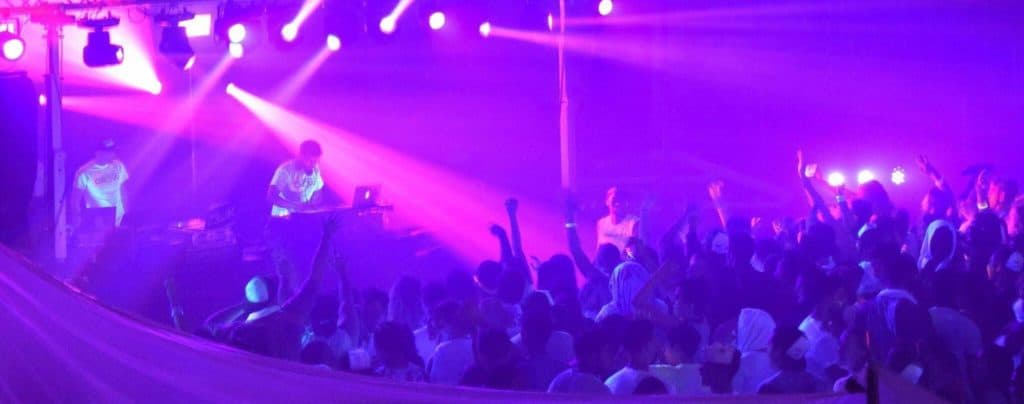 Elevated DJ performing at Operation Glow dance event with vibrant purple lighting.