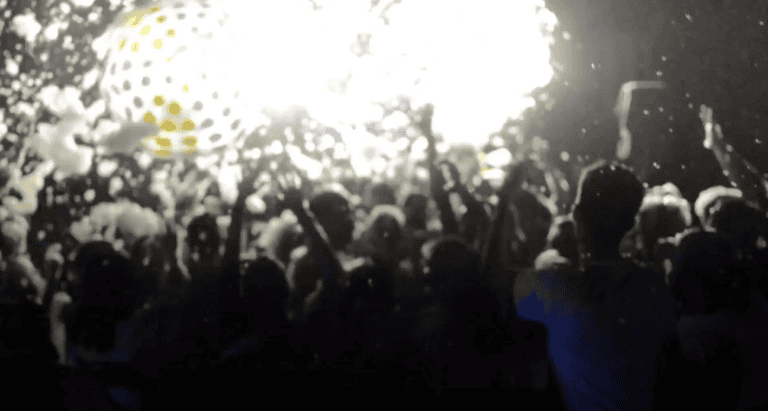 A vibrant crowd enjoying a glow-themed event with colorful lights and energetic atmosphere.