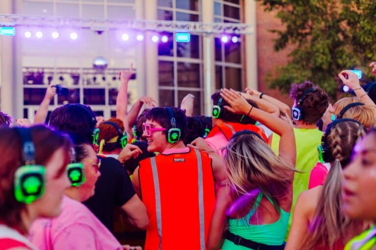 Jumping crowd at an outdoor dance event with colorful headphones and vibrant attire.